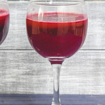 A glass of pomegranate juice with another glass on the side.