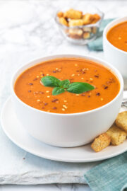 a bowl of roasted tomato soup garlished with basil and chili flakes with croutons on side.