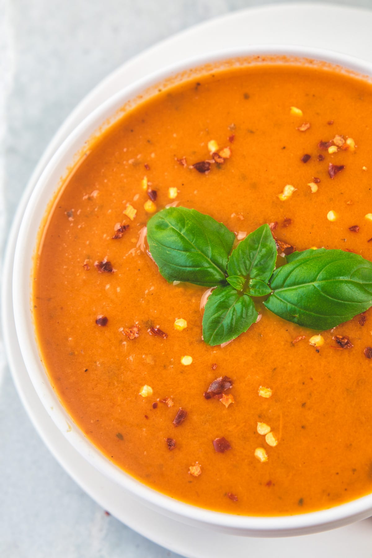 Top voew of roasted tomato soup in a bowl garnished with basil leaves and chili flakes.