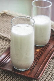 2 glasses of salted lassi on a wooden tray with napkin underneath.