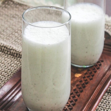 2 glasses of salted lassi on a wooden tray with napkin underneath.