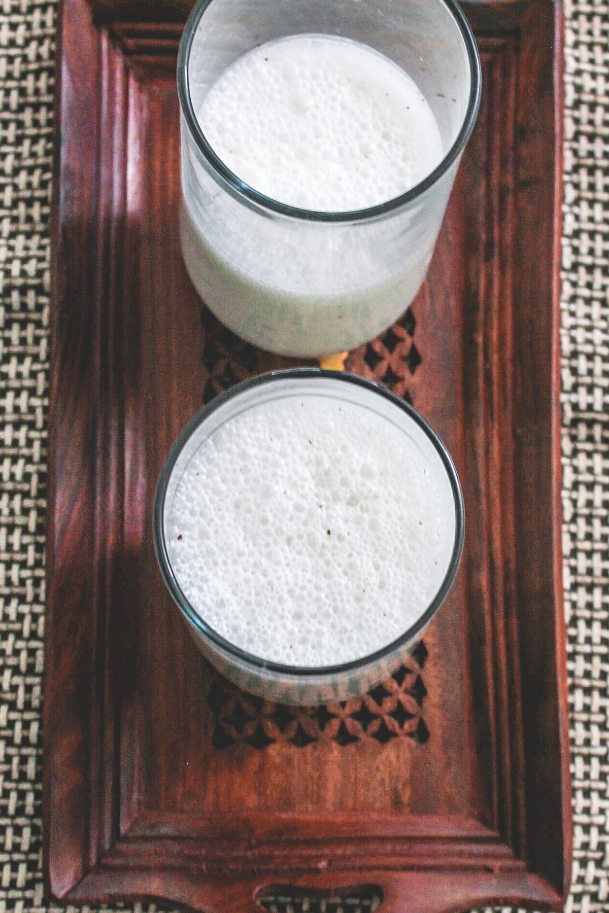 Salted lassi served in 2 glasses in a wooden tray.