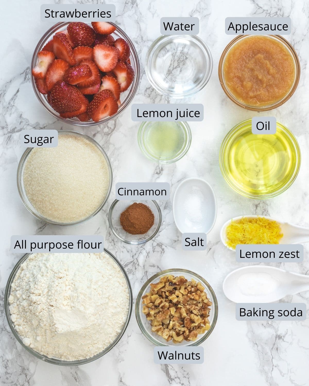 Ingredients used in strawberry bread with labels on marble surface.