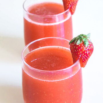 2 glasses of strawberry juice garnished with a whole strawberry.