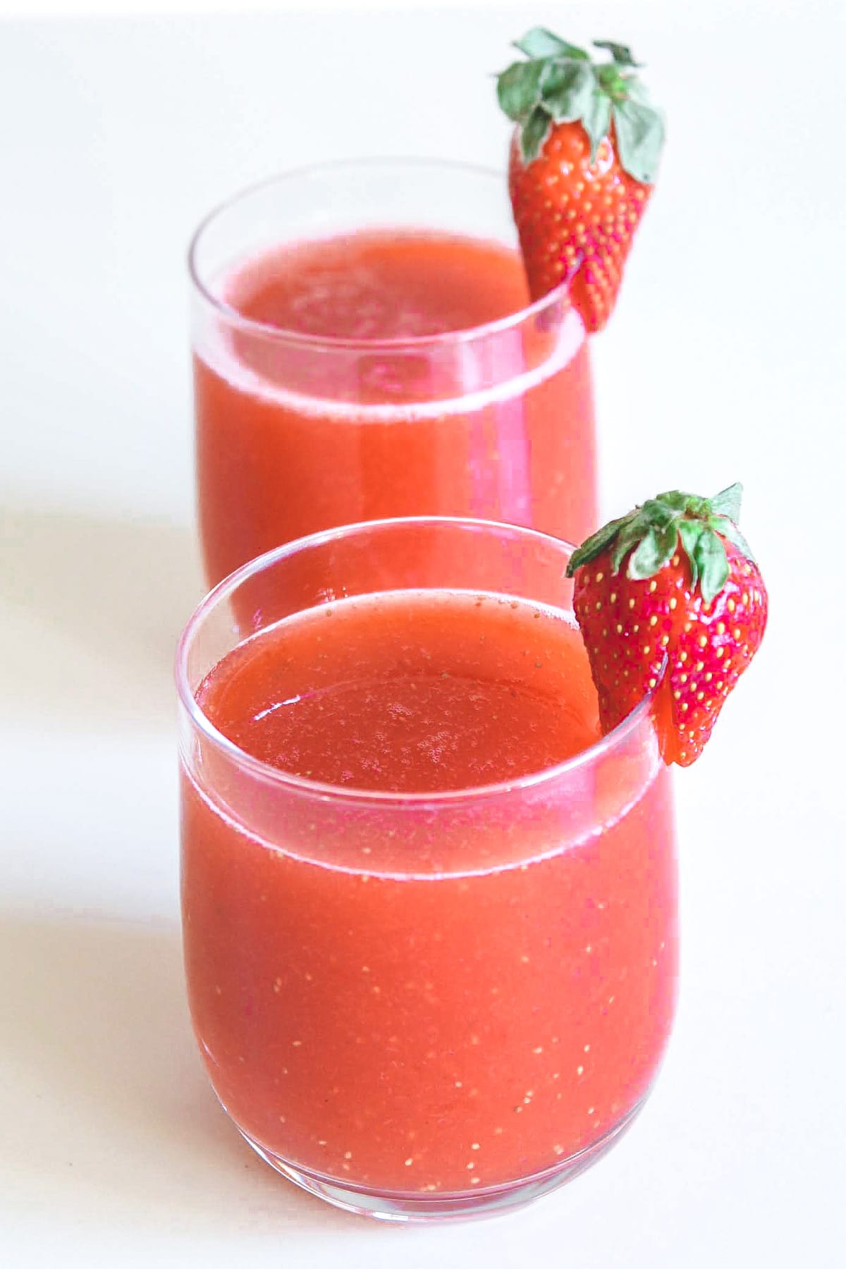 2 glasses of strawberry juice garnished with a whole strawberry.