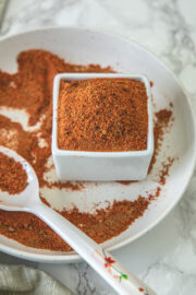 Tikka masala spice mix in a sqaure bowl with some masala in a spoon and plate.