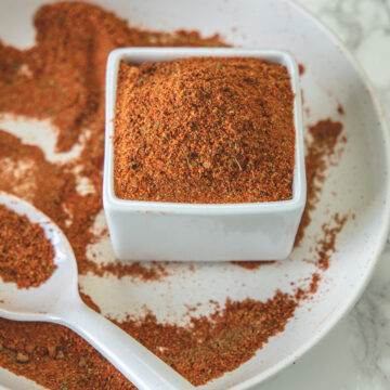 Tikka masala spice mix in a sqaure bowl with some masala in a spoon and plate.