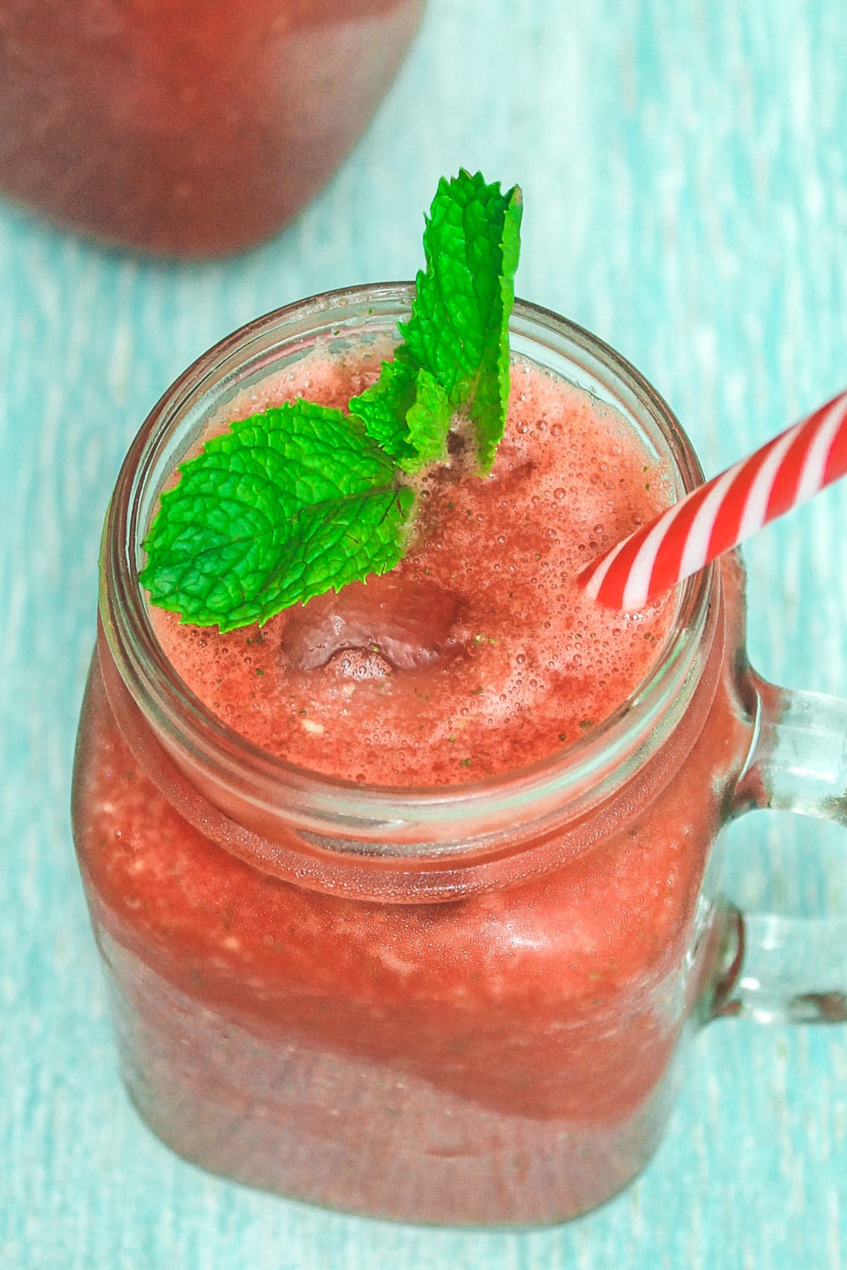 watermelon mint juice in mason jar cup with a straw and mint leave garnish.