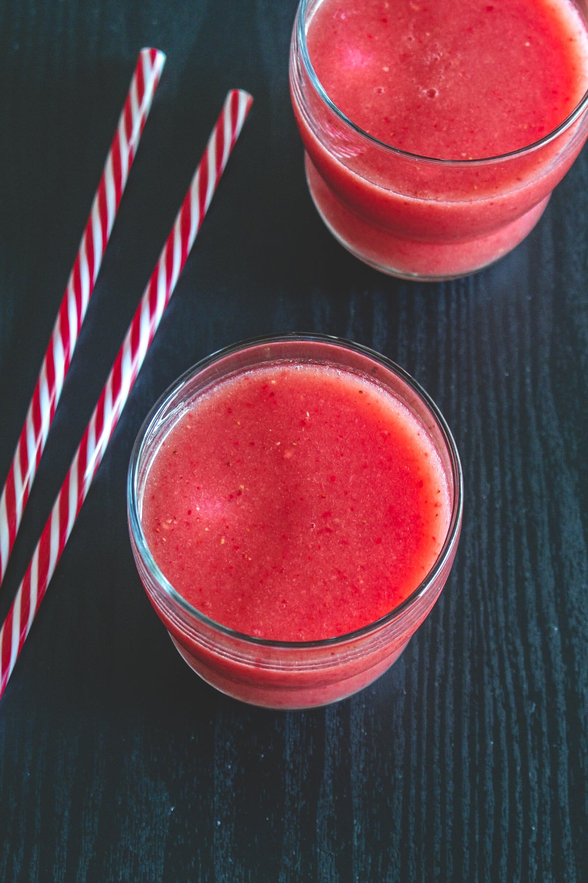 2 glasses of strawberry watermelon juice with 2 red strip straws on left.