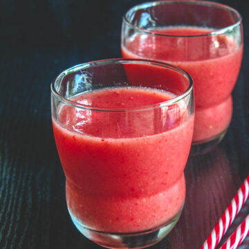 2 glasses of strawberry watermelon juice with 2 straws on the side.