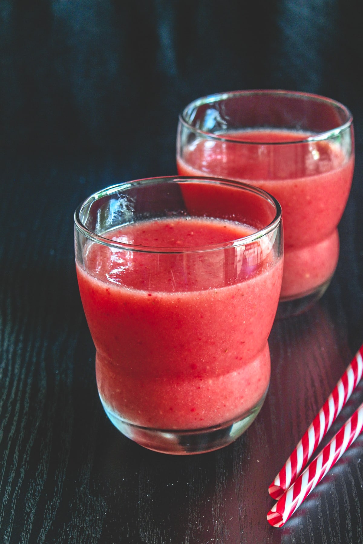 2 glasses of strawberry watermelon juice with 2 straws on the side.