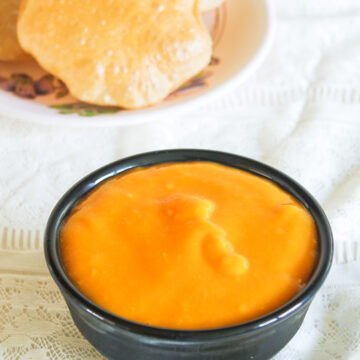 A bowl of aamras with puri in the back.