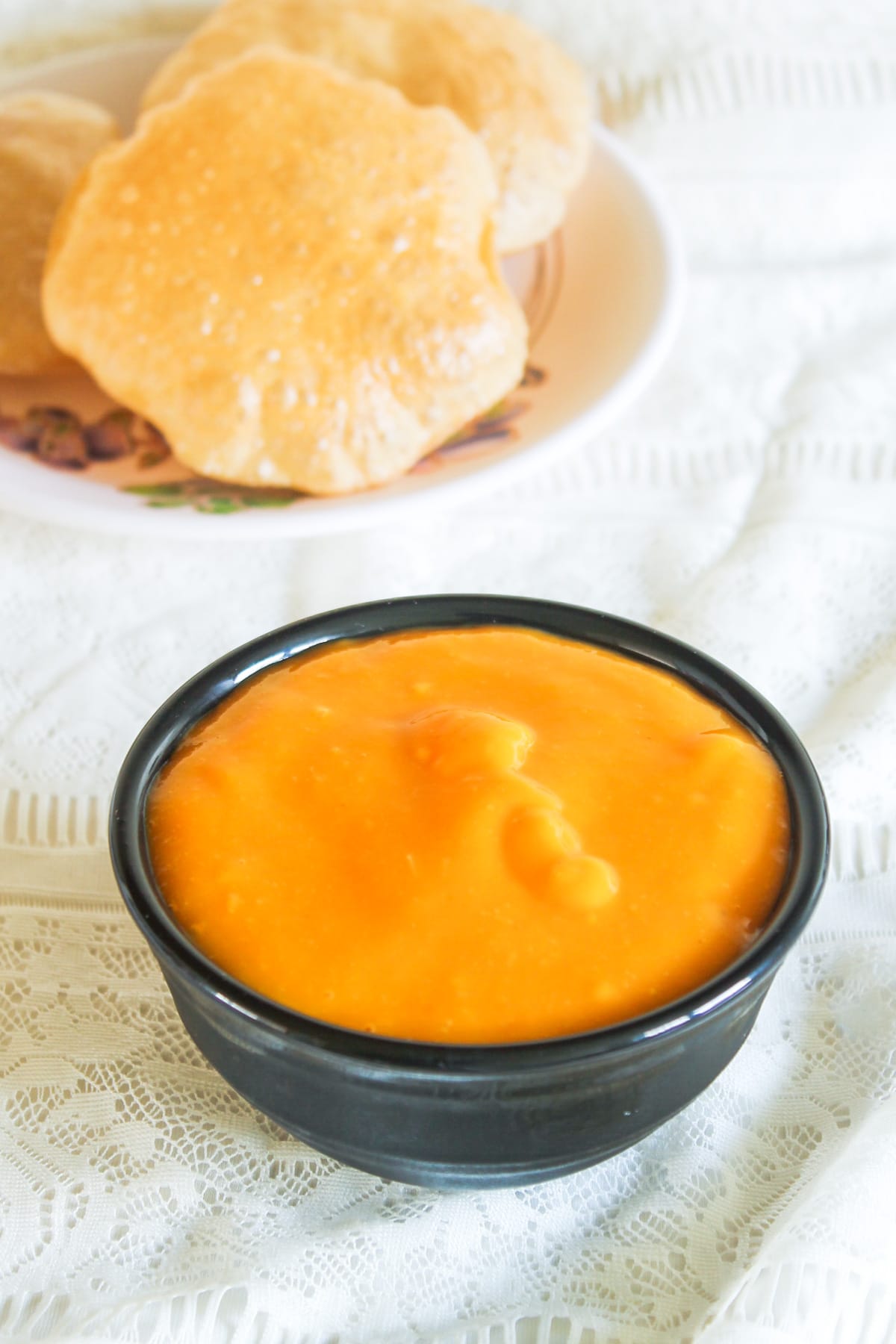 A bowl of aamras with puri in the back.