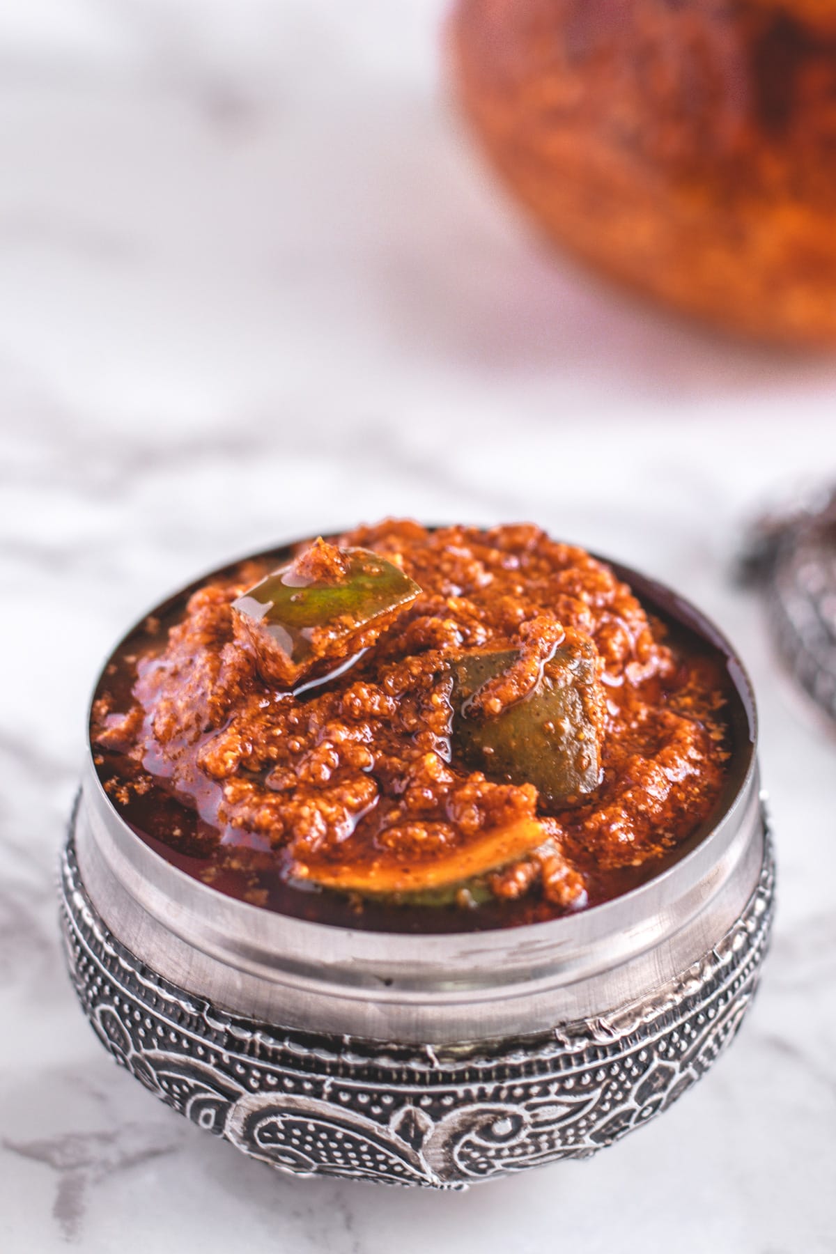 Avakaya pachadi in a serving bowl with lid and extra pickle in the back.