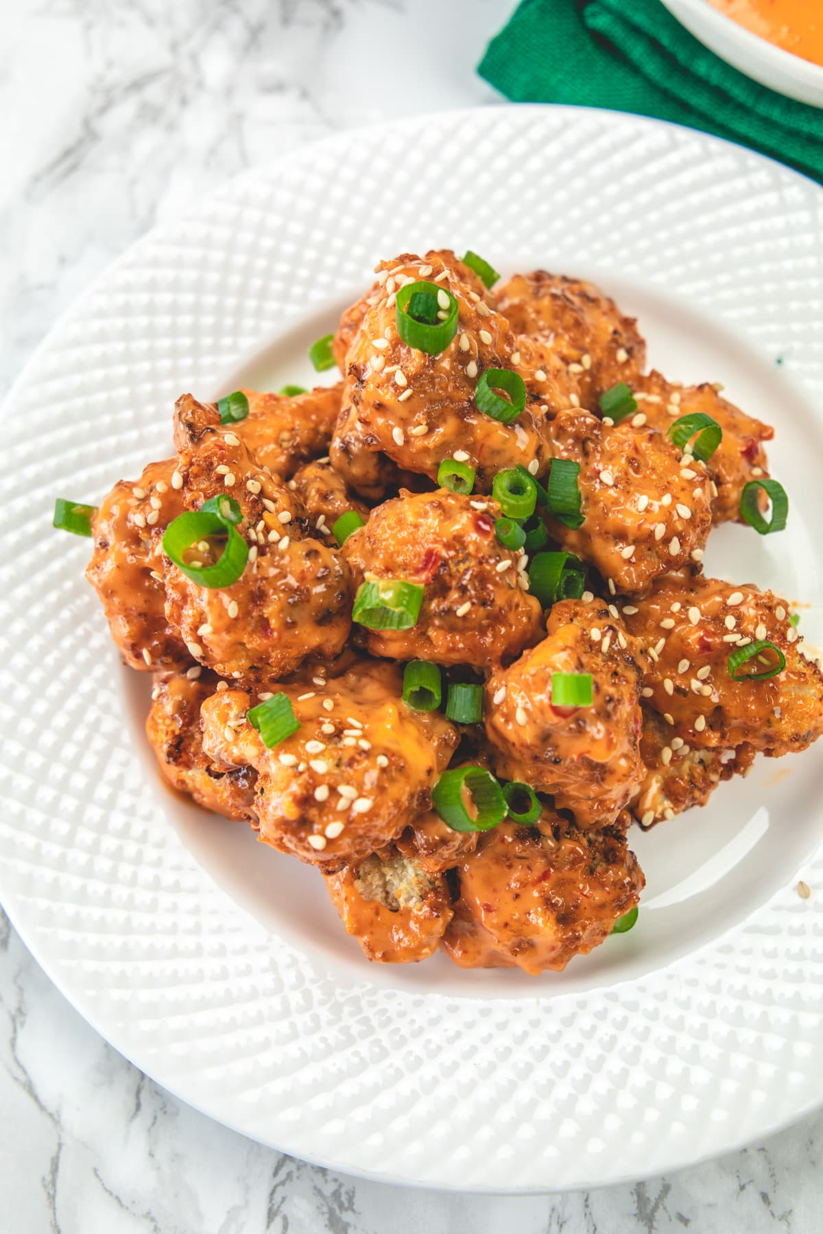 Bang bang cauliflower served in a plate, garnished with spring onion greens and sesame seeds.