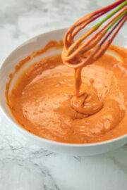 Drizziling the bang bang sauce back in a bowl using a whisk.