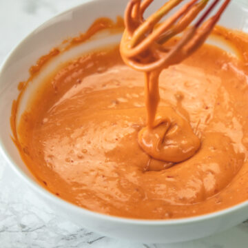 Drizziling the bang bang sauce back in a bowl using a whisk.