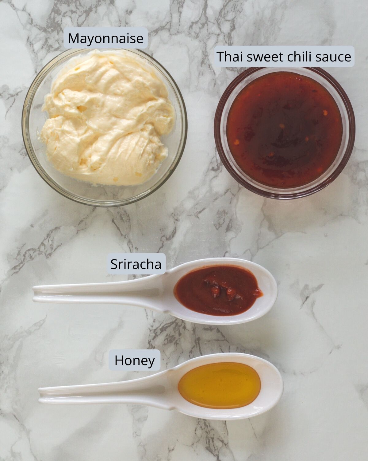 Ingredients used for making bang bang sauce recipe with labels on marble background.