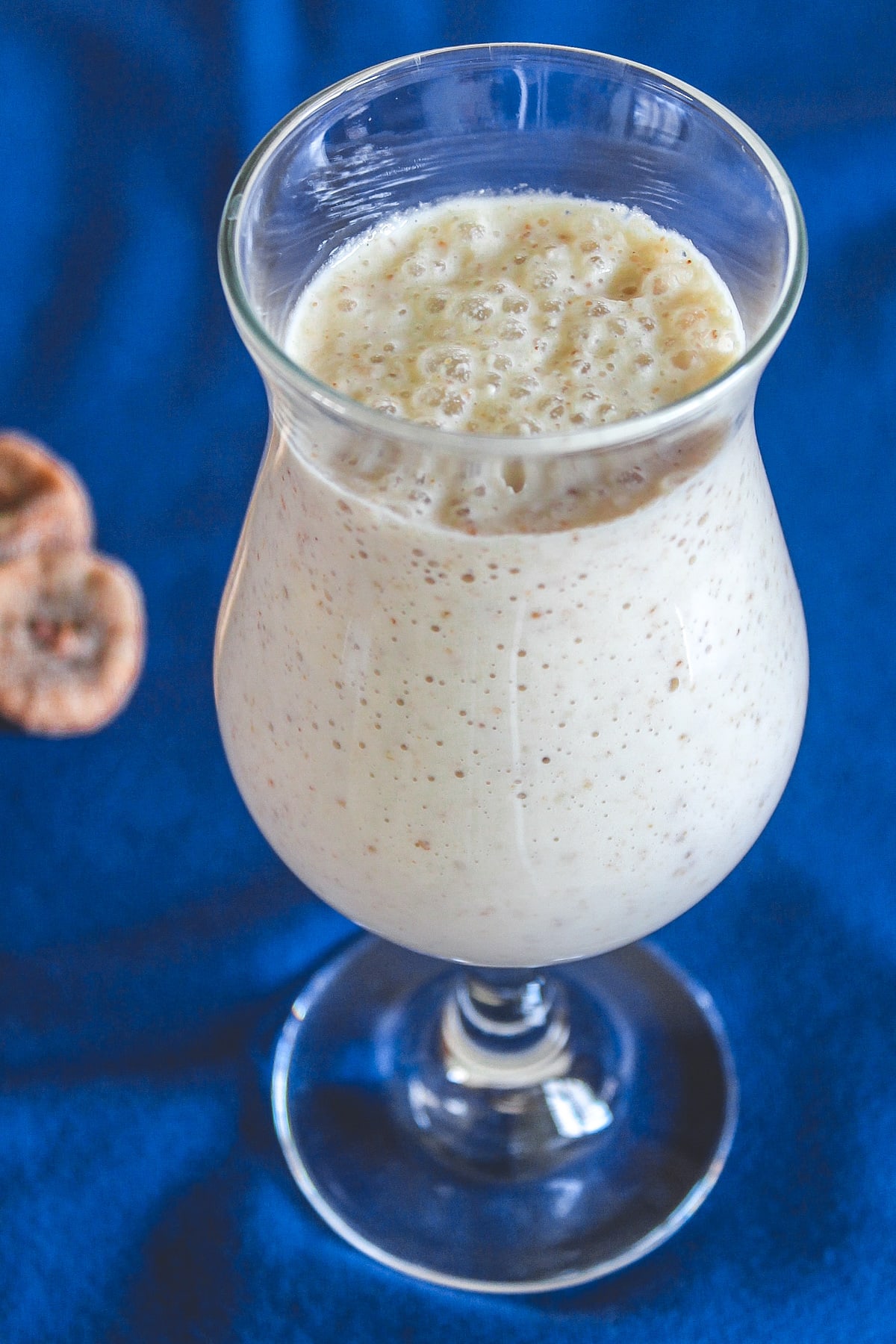 A glass of kaju anjeer milkshake with a few dried figs in the back side.