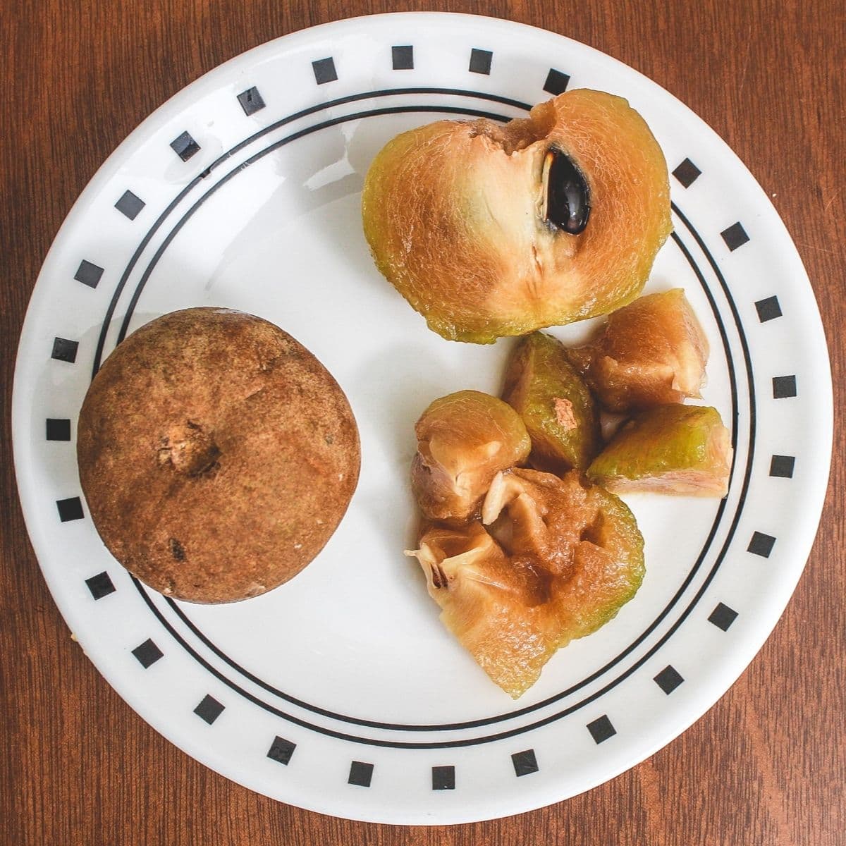 Whole chikoo, sliced into half and chopped in a plate.