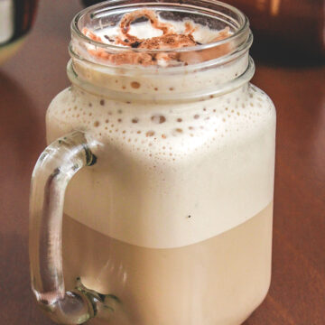 Cold coffee in a mason jar mug with coffee container in the back.