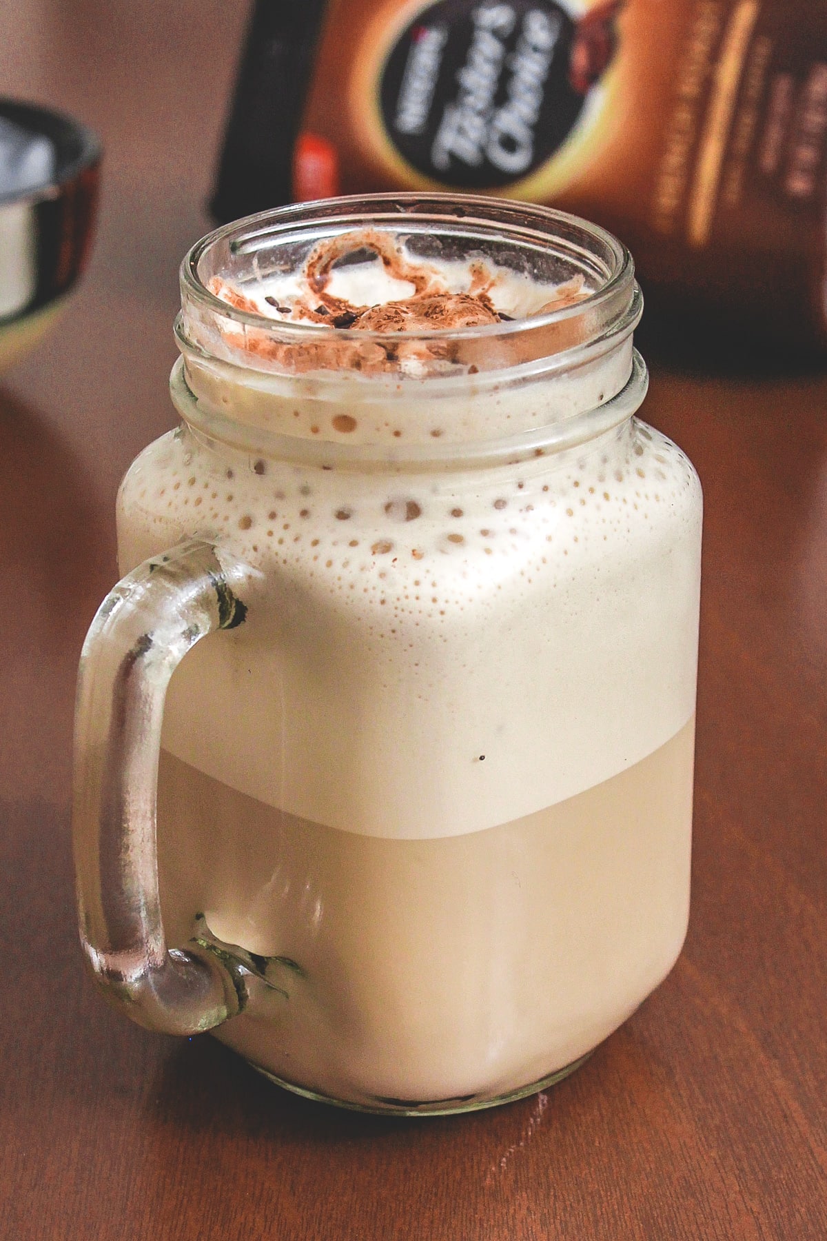 Cold coffee in a mason jar mug with coffee container in the back.