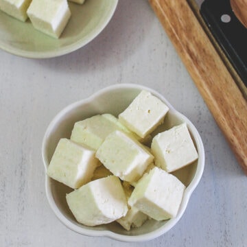 Paneer cubes in a bowl with few more cubes in back.