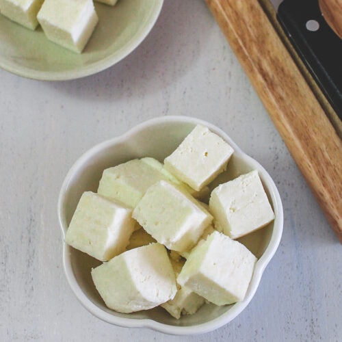 Paneer cubes in a bowl with few more cubes in back.
