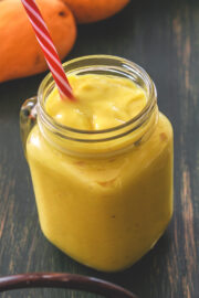 Mango banana smoothie in a mason jar mug with a straw.