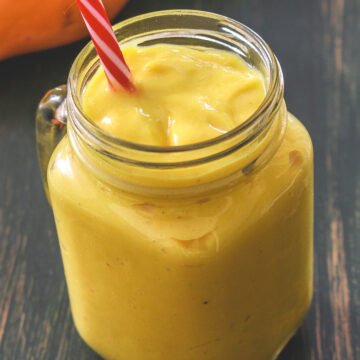 Mango banana smoothie in a mason jar mug with a straw.