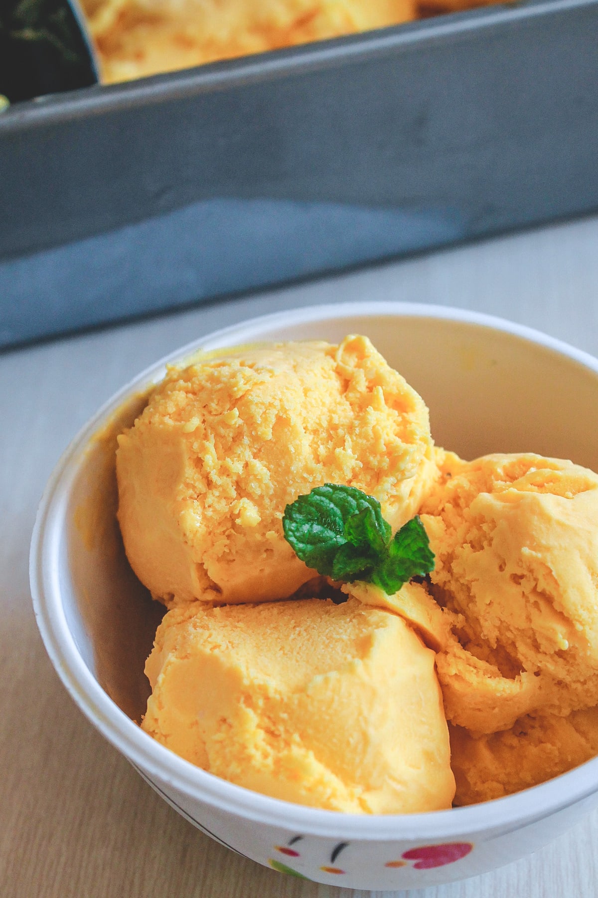 3 scoop of mango ice cream garnished with mint leaves.