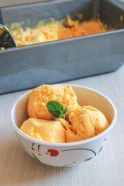 3 scoops of mango ice cream in a bowl and garnished with a mint leaf with loaf pan in back.