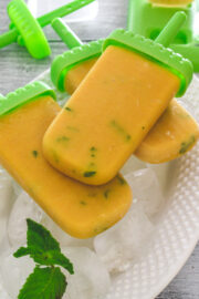 3 mango popsicles on the tray of ice cubes with mint leaves on the side.
