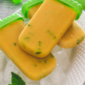 3 mango popsicles on the tray of ice cubes with mint leaves on the side.