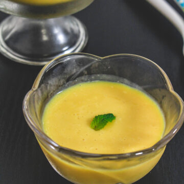 Mango pudding in a bowl garnished with mint leaf.