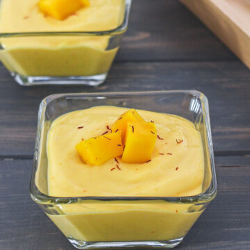 2 bowls of manngo shrikhand garnished with mango pieces and saffron.