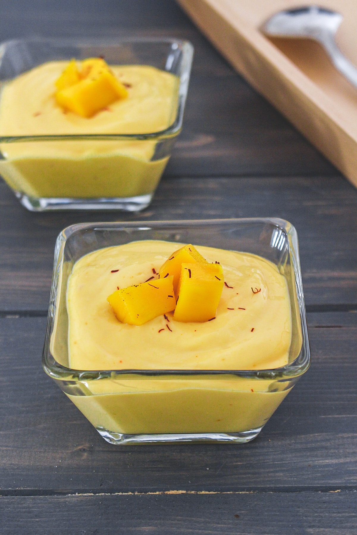 2 bowls of manngo shrikhand garnished with mango pieces and saffron.