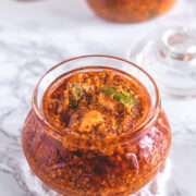 Methia keri mango pickle in a glass jar with more pickle in background.