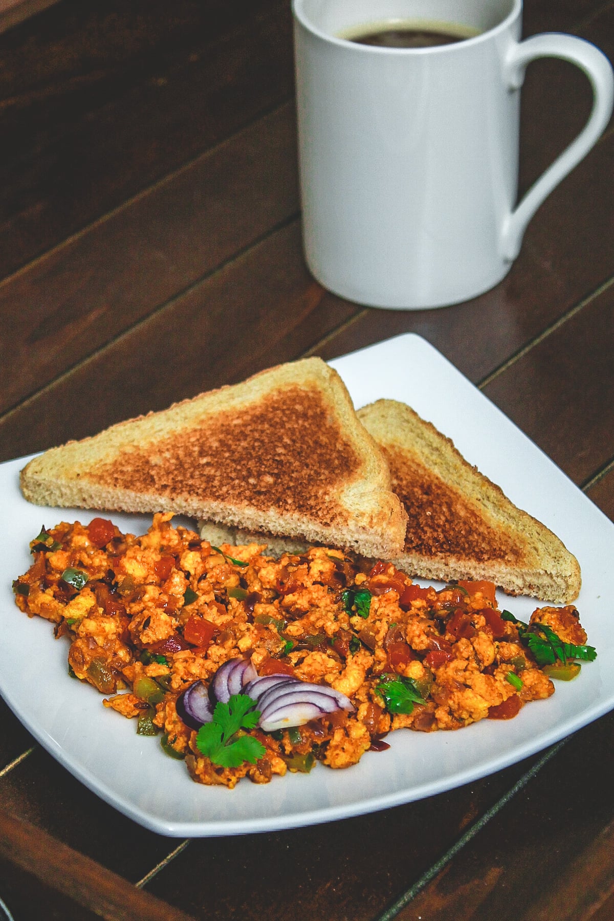 Paneer bhurji with toasted bread triangles in a plate with a cup of coffee.