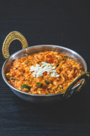 Paneer bhurji gravy in kadai serving bowl with raw grated paneer sprinkled on top.