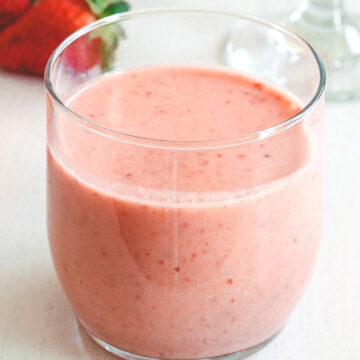 A glass of strawberry banana smoothie with banana and strawberries in the back.
