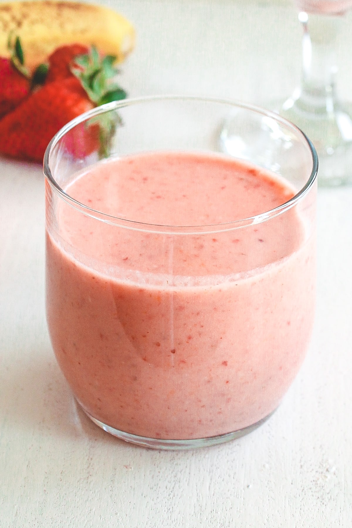 A glass of strawberry banana smoothie with banana and strawberries in the back.