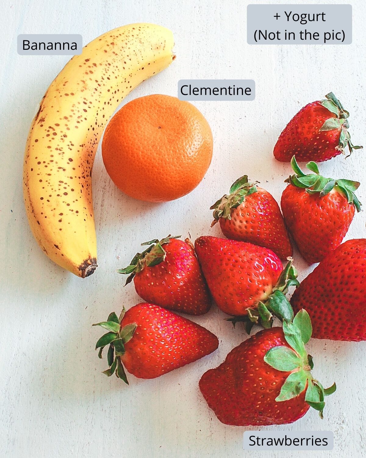 Banana, clementine and strawberries with labels on white board.