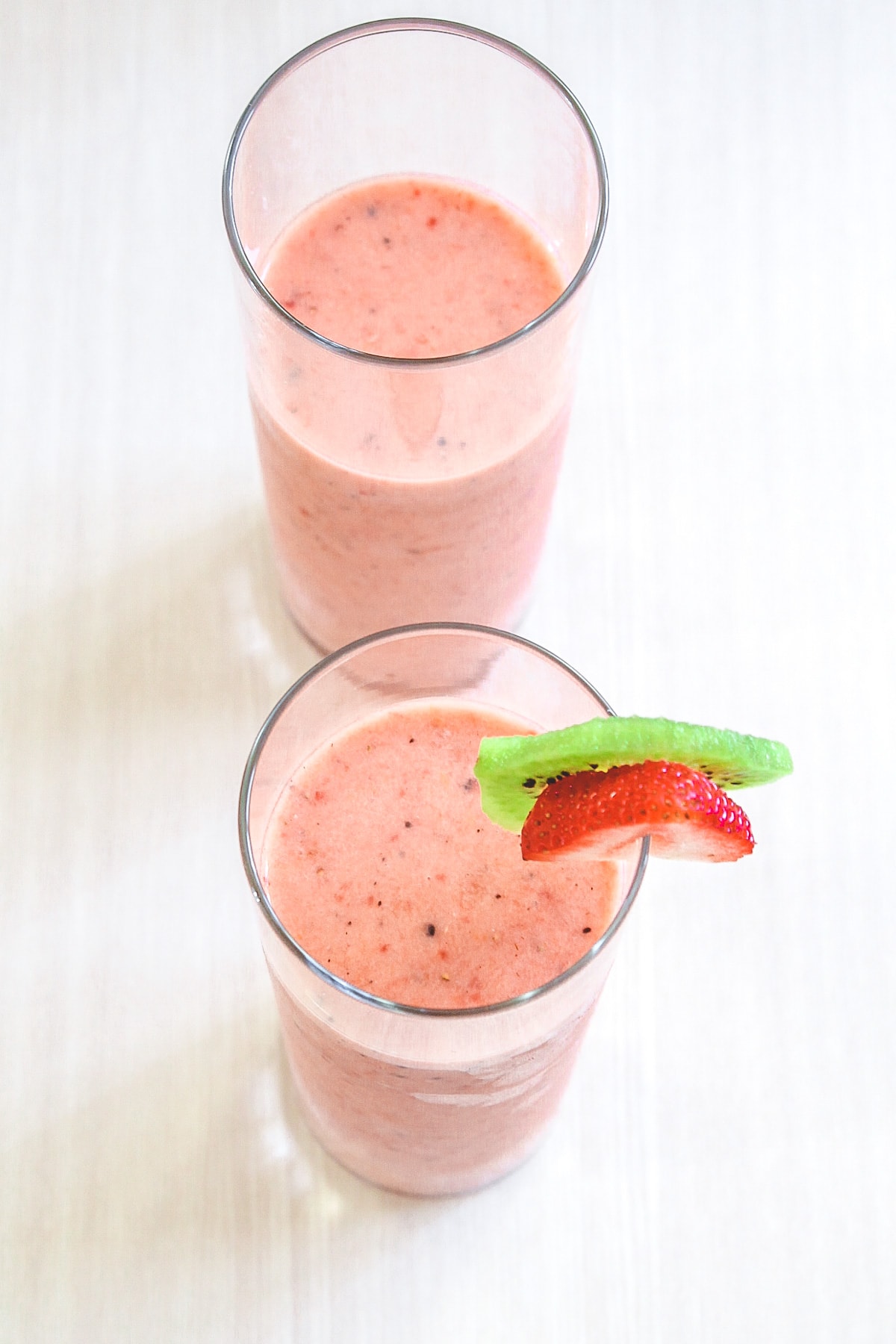 2 glasses of strawberry kiwi smoothie and one glass garnished with slice strawberry and kiwi.
