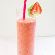 Strawberry kiwi smoothie in a glass with a straw and garnished with slices of strawberry and kiwi.