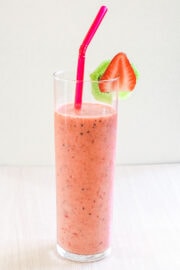 Strawberry kiwi smoothie in a glass with a straw and garnished with slices of strawberry and kiwi.