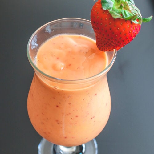 A glass of strawberry mango smoothie garnished with a whole strawberry.