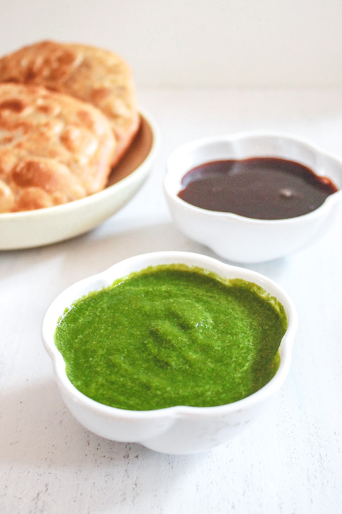 Green chutney bowl with meethi chutney bowl and kachori in the back.