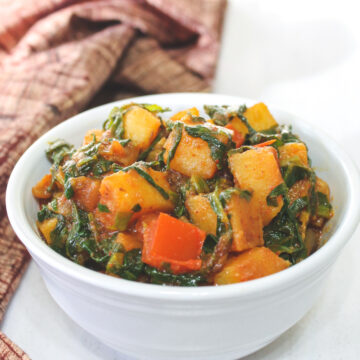 Palak sabzi in a white bowl with brown napkin on the side.