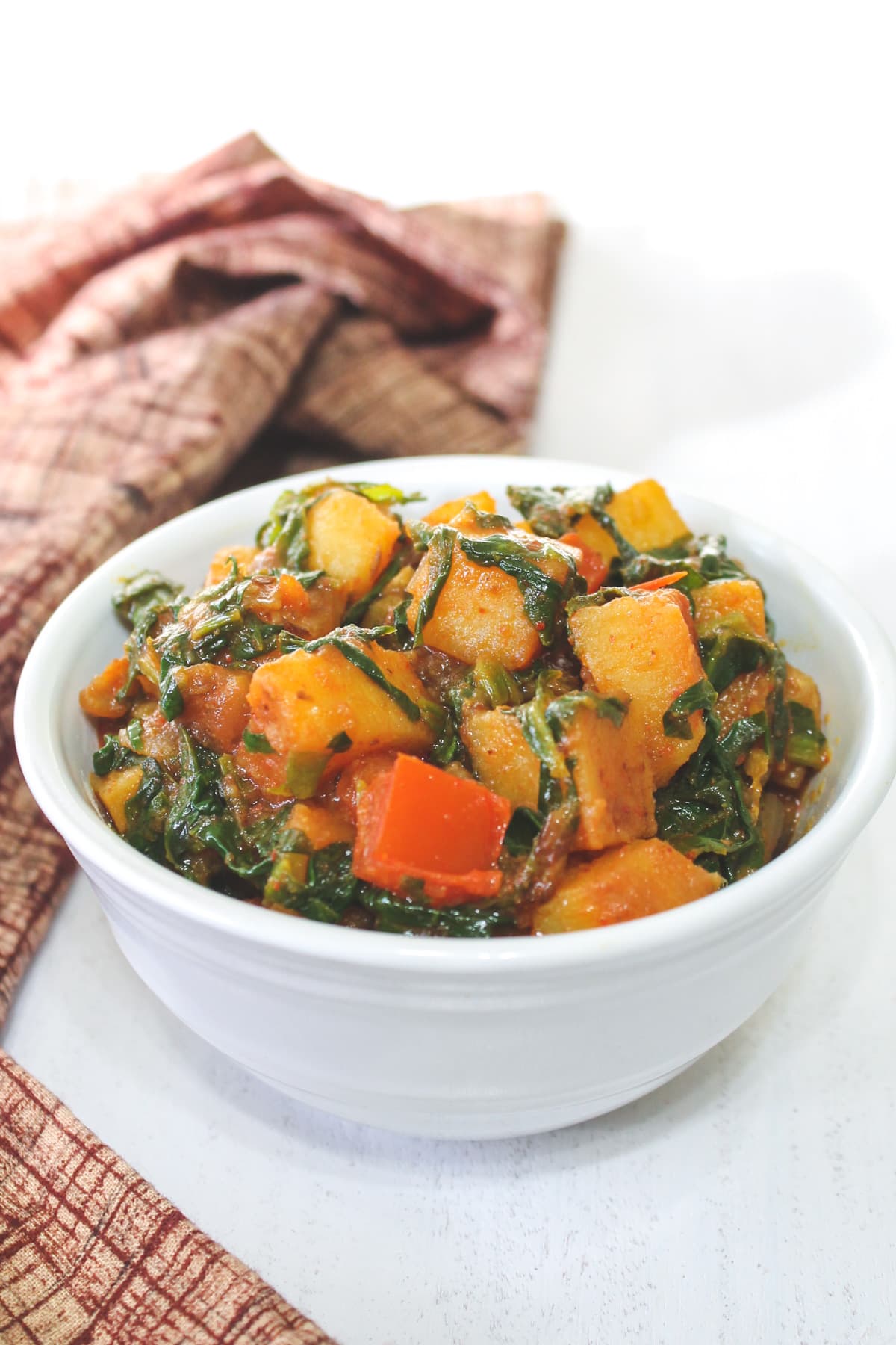 Palak sabzi in a white bowl with brown napkin on the side.